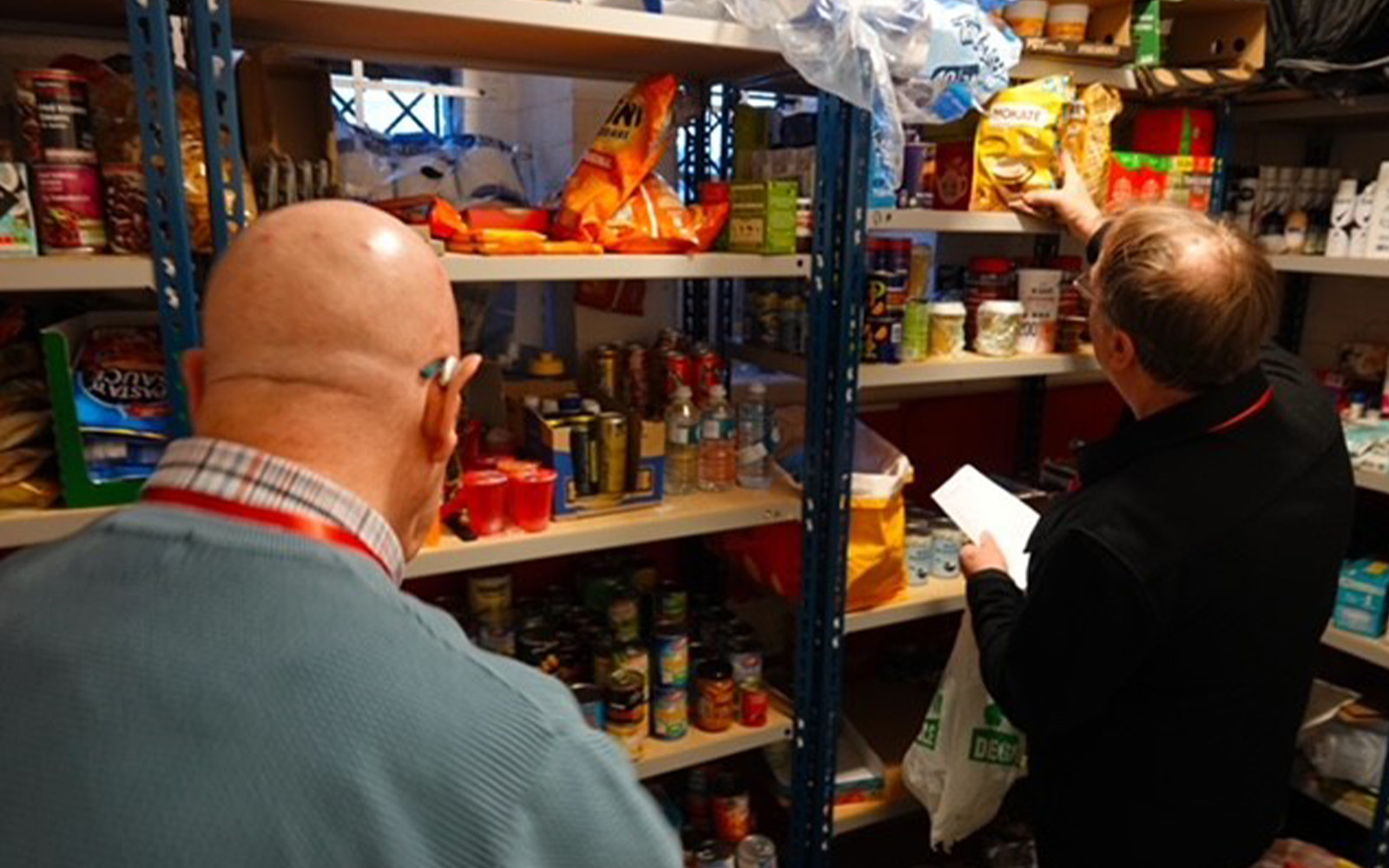 Two volunteers with the shelves of food used to feed the homeless
