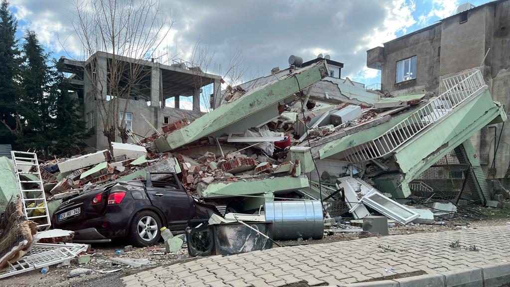 The aftermath of the devastating earthquake showing collapsed buildings and a crushed car.