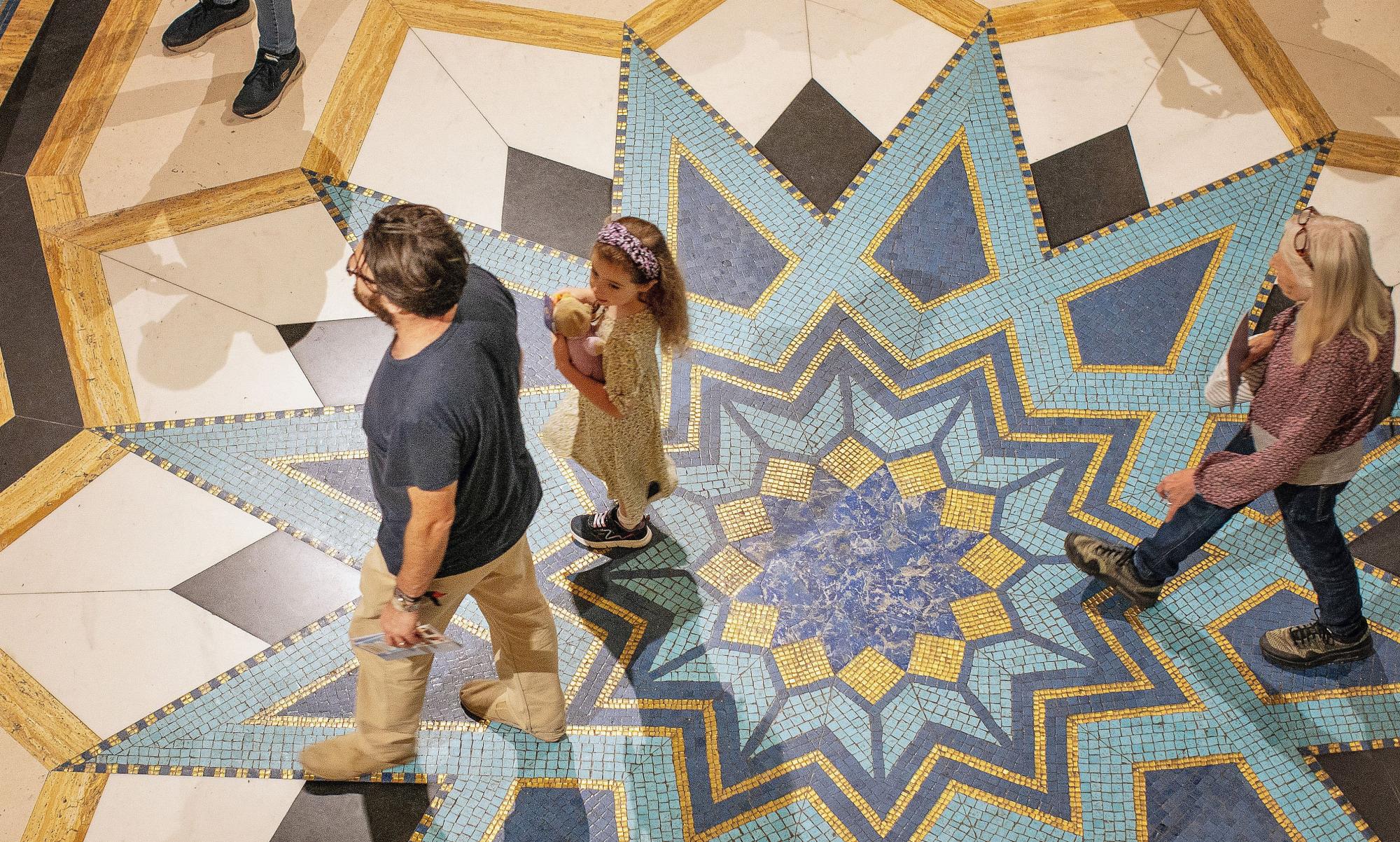 Visitors to Freemasons' Hall. The photo is of a man, a wom and a young girl, taken from above as they walk across art deco marble flooring.