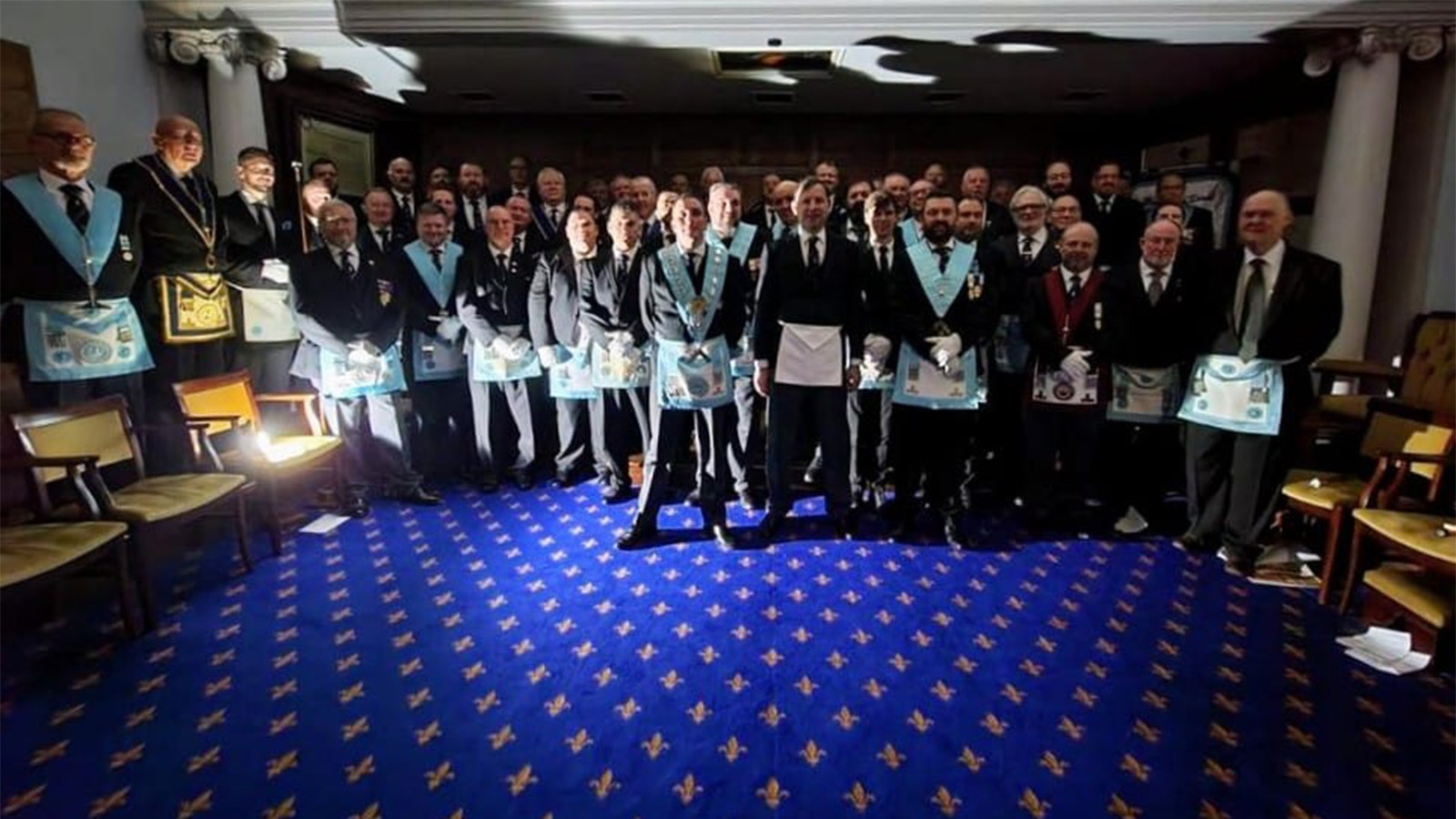 The Three Pillars Club all Stand in a dark room lit by a torch at the front left hand side of the group.