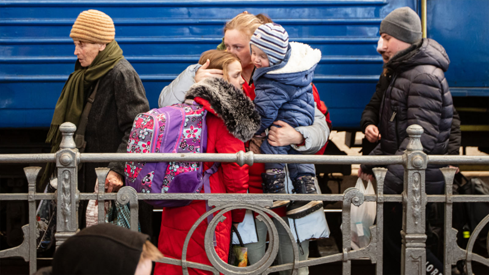  A woman stands behind a railing holding her two young children