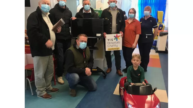 joseph in a red battery powered car, with hospital staff and members of donating lodges