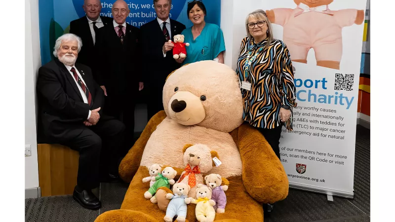 A group of people stood around a giant teddy bear in front of the TLC banner.